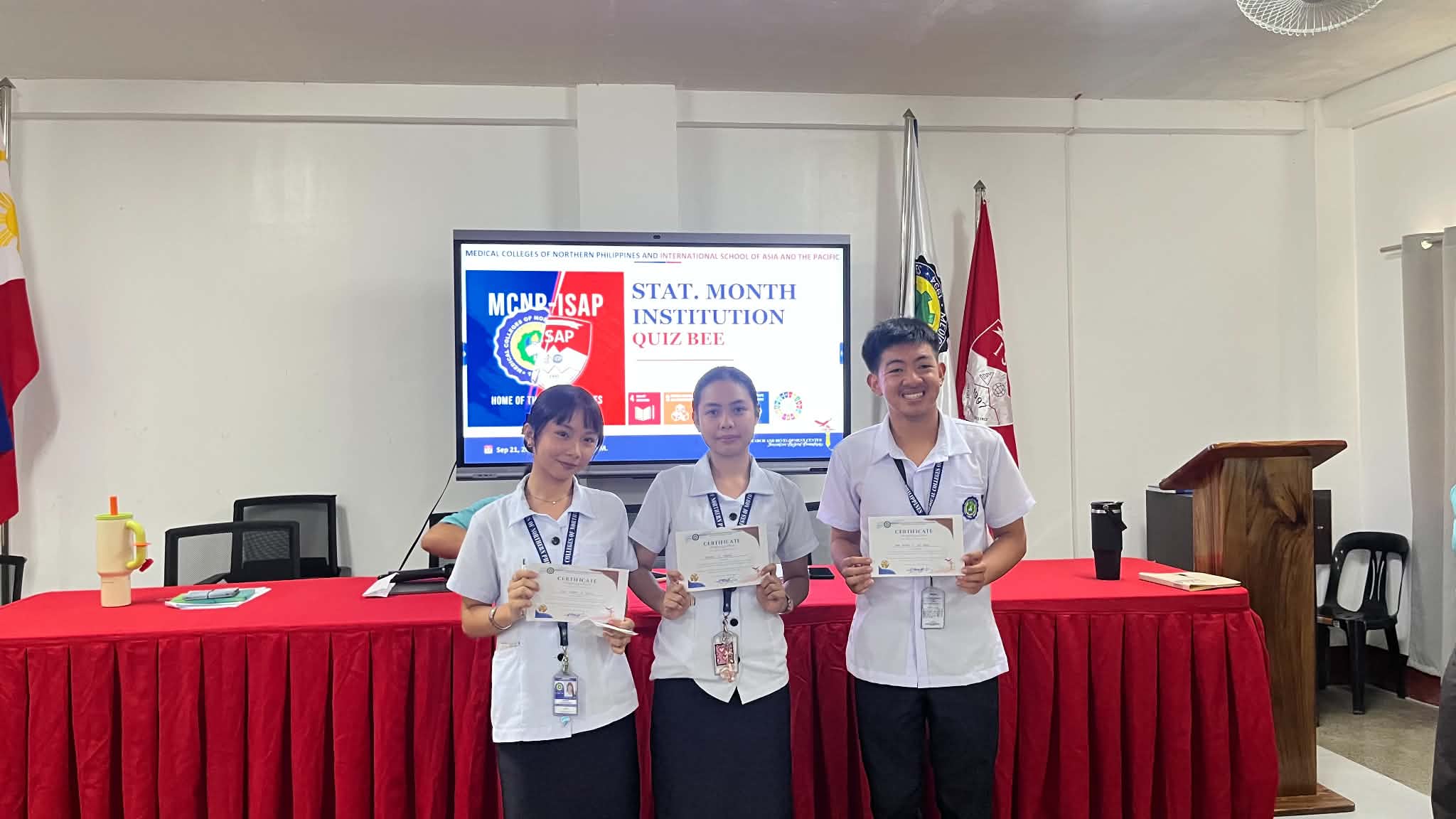 MCNP Quiz Bee Winners holding certificates in front of the official backdrop